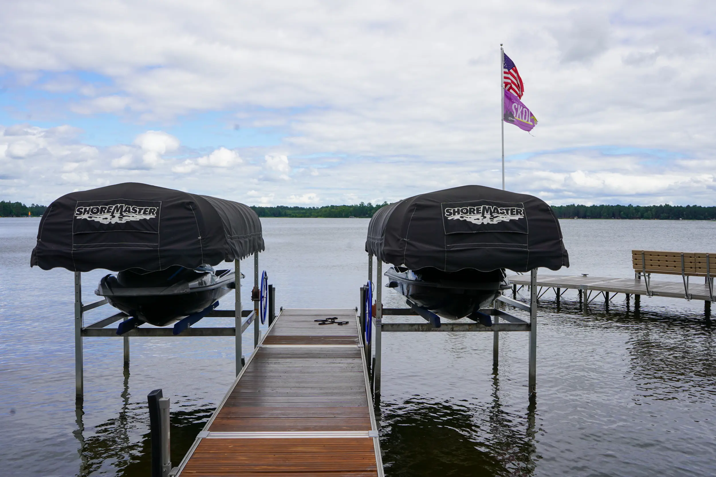 Two covered jet skis on ShoreMaster PWC lifts beside a lake dock